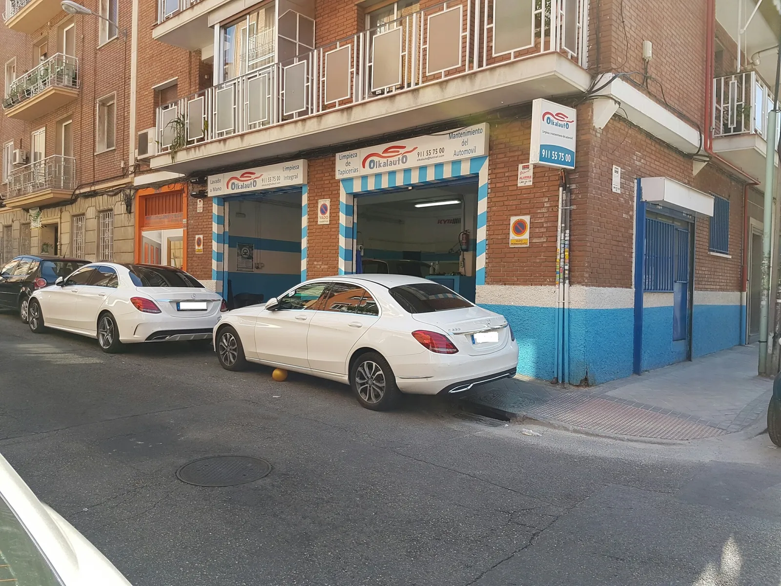 La esquina de Olkalauto: dos naves con el rótulo azul y blanco y dos coches blancos aparcados delante
